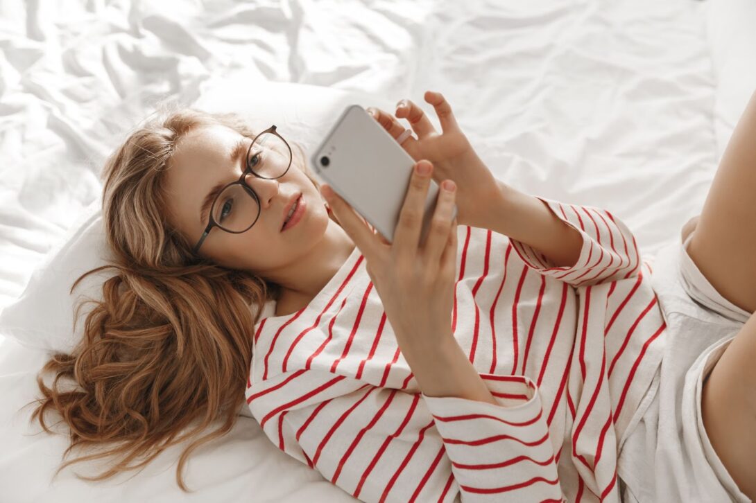 Girl with glasses lies on the bed and texts