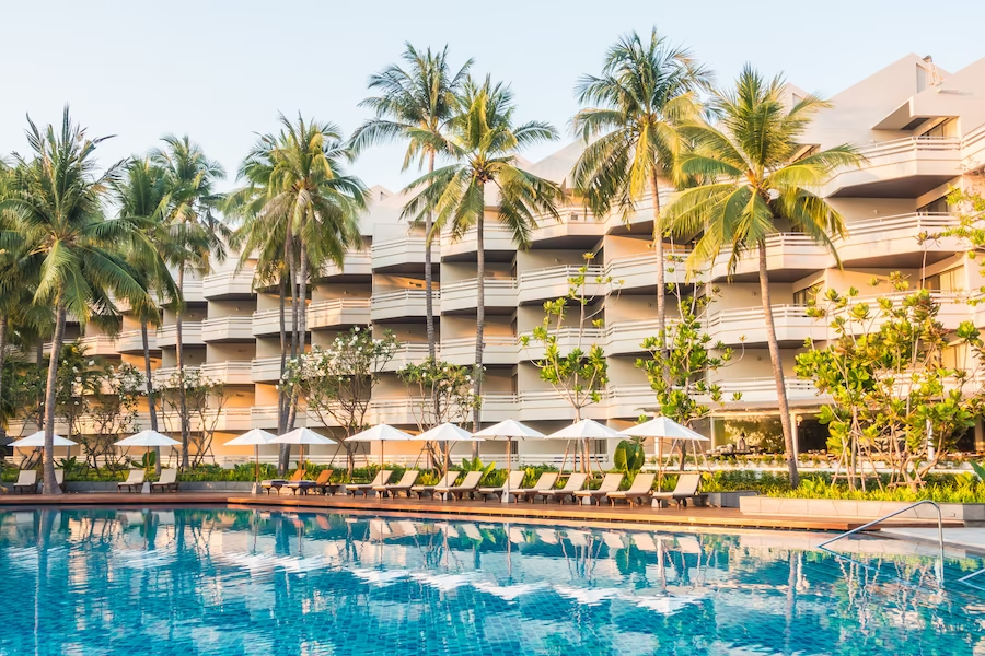 Exterior view of a hotel with a swimming pool and coconut trees in the surroundings