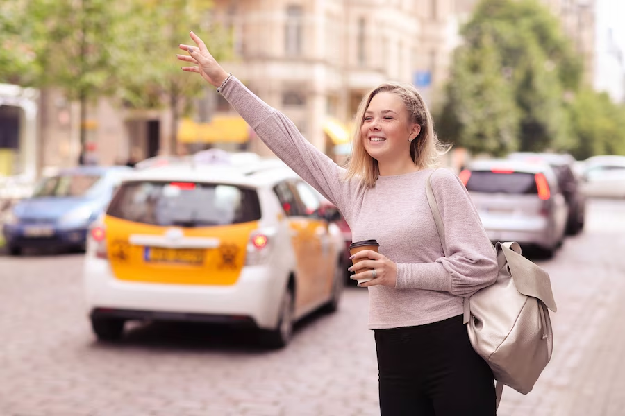 Woman on the street holding a cup, raising her hand as if signaling for a taxi