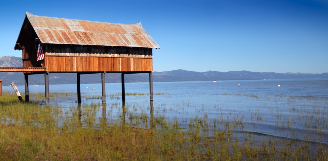 Hut on water with plants, mountains, and sky