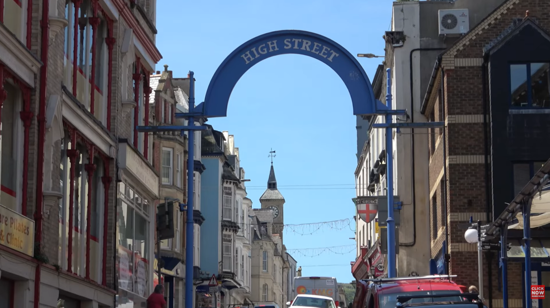 a city view of the buildings and church, high street sign above