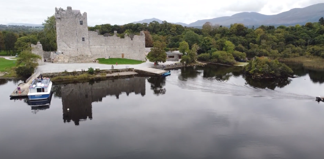 Image of Muckross House and Gardens by the lake, boat parked, surrounded by numerous trees