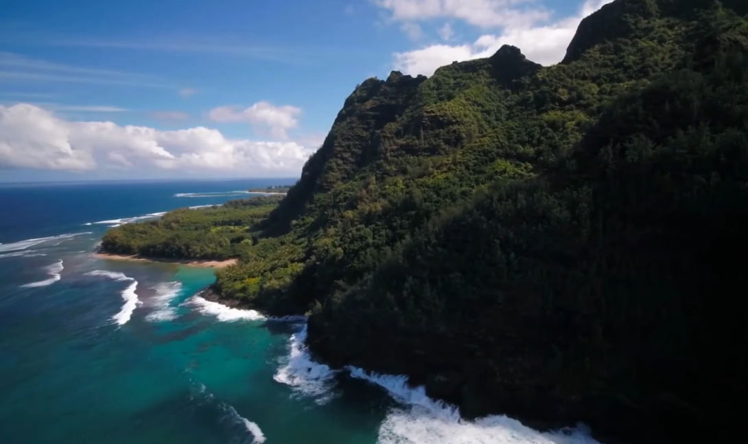 an island with trees on it, ocean and waves, and cloudy blue sky