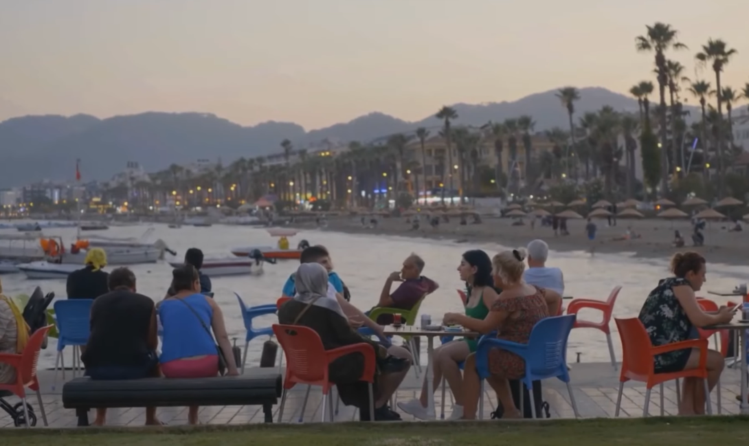 people sitting on chairs near the beach, palms, and beach umbrellas