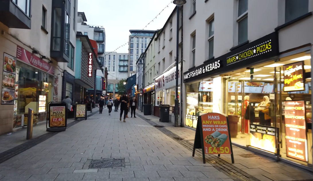 a city street with shops and restaurants, people on the street, and Haks sign near building