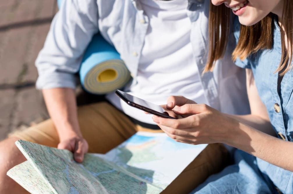 man and woman sitting outside and holding map and phone in hands