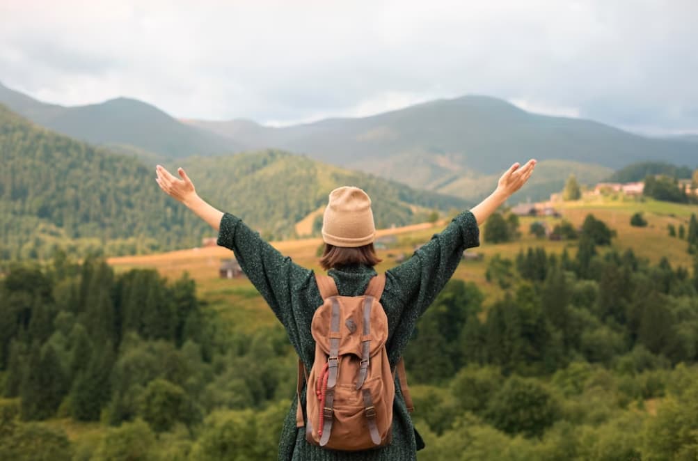 A woman with outstretched arms enjoys the view of green hills