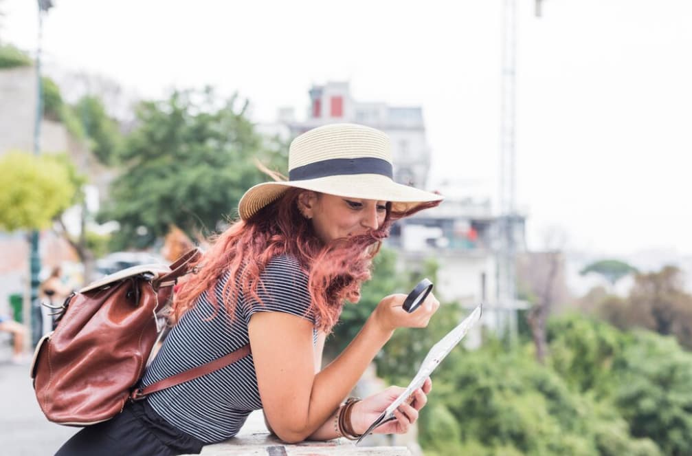 A woman with a hat checks her phone while holding a map