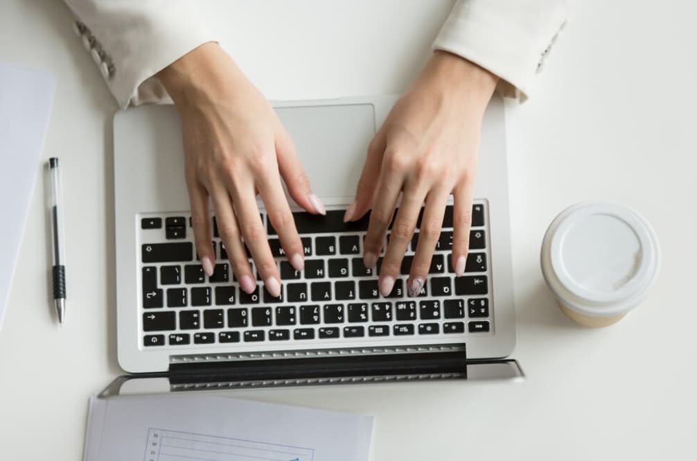 Overhead view of hands typing on a laptop next to a coffee cup